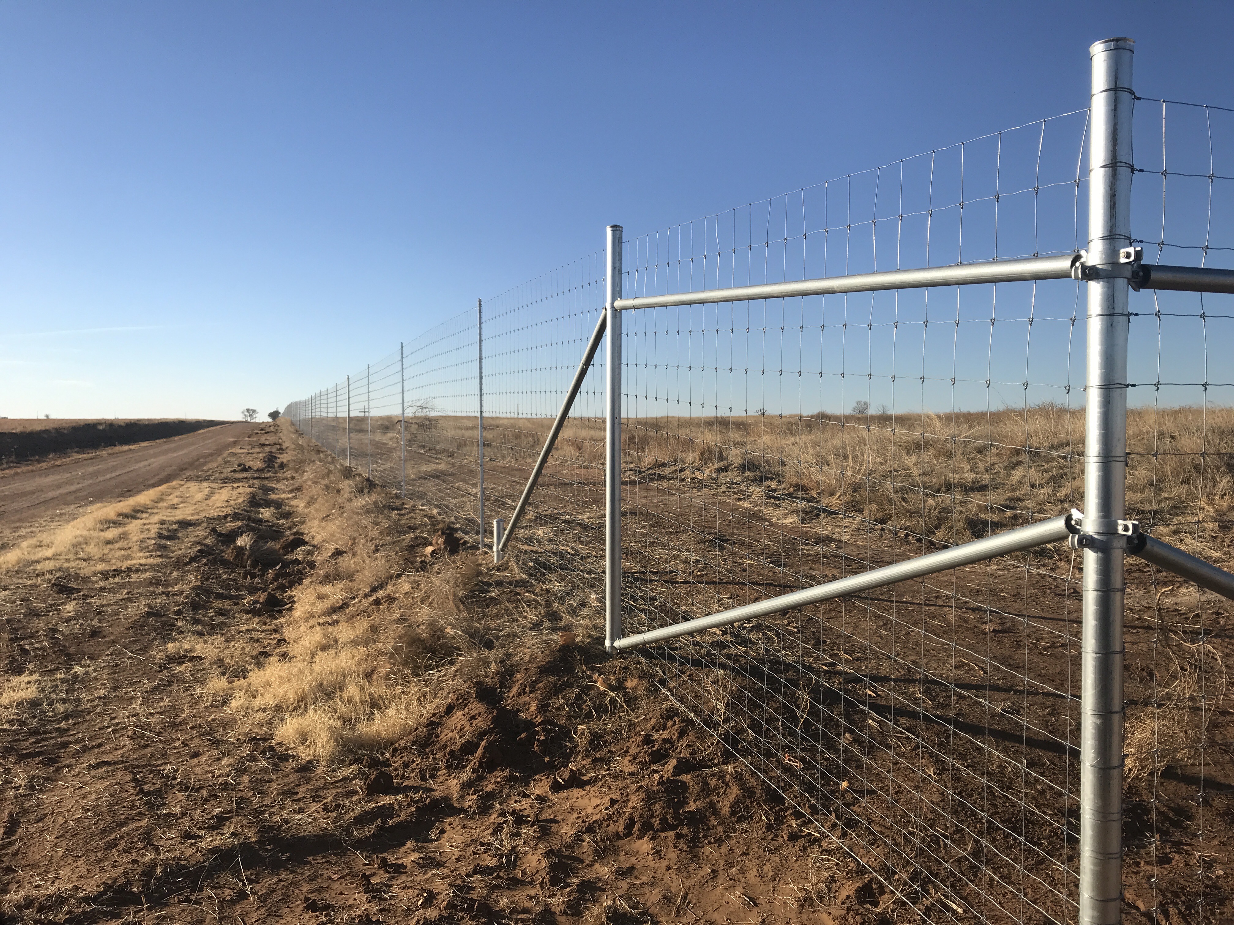 J4 high game fence with steel posts and a braced assembly beside a ranch road.