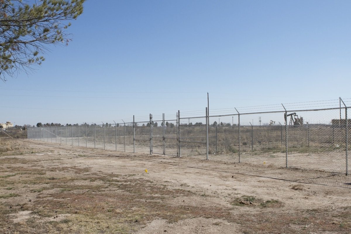 Galvanized chain-link perimeter with barbed wire and double gates at a West Texas commercial site